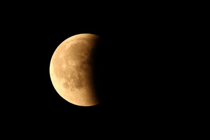 Halbmond auf schwarzem Hintergrund, orangefarbene Tönung und lichte Details sichtbar.