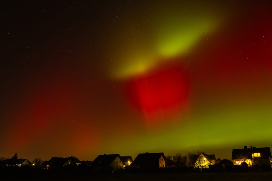 Nordlichter erleuchten den Nachthimmel über einem Wohngebiet mit beleuchteten Häusern.