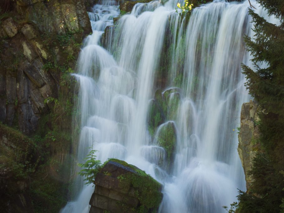 Einmaliger Wasserfall mit fließendem Wasser und umgebenden grünen Felsen und Bäumen.