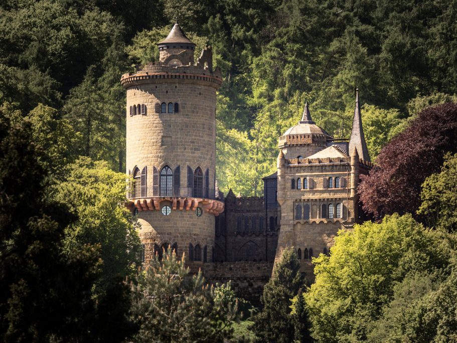 Mittelalterliches Schloss umgeben von dichten, grünen Wäldern.