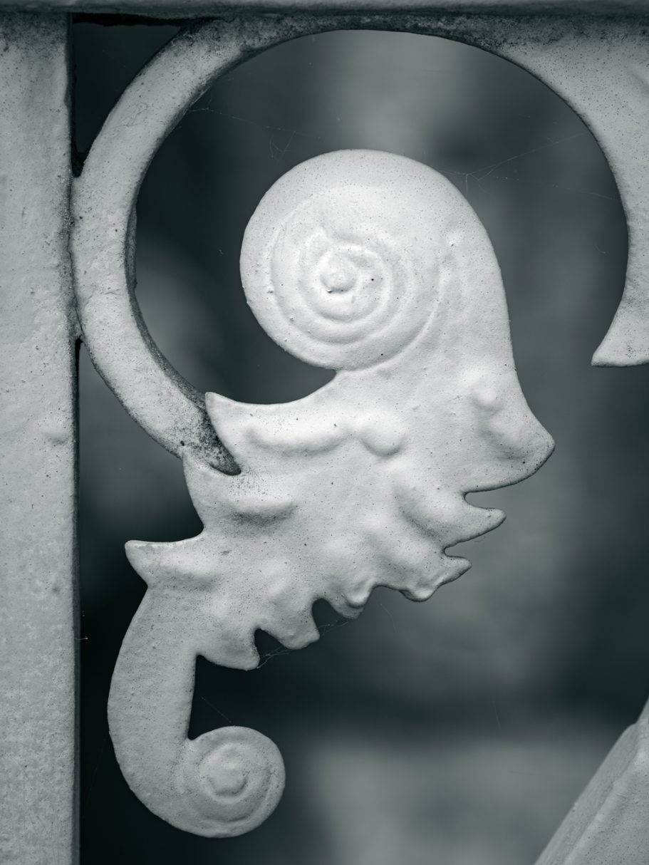 Detail eines geschwungenen metallenen Geländers mit einer spiraligen Verzierung.