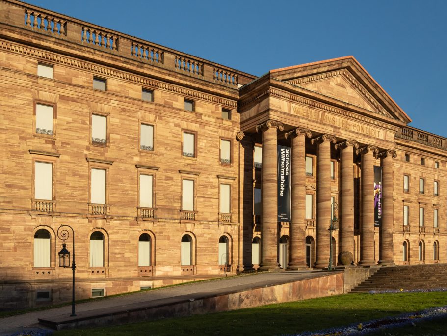 Historisches Gebäude mit Säulen und rotem Sandstein in der Abendsonne.